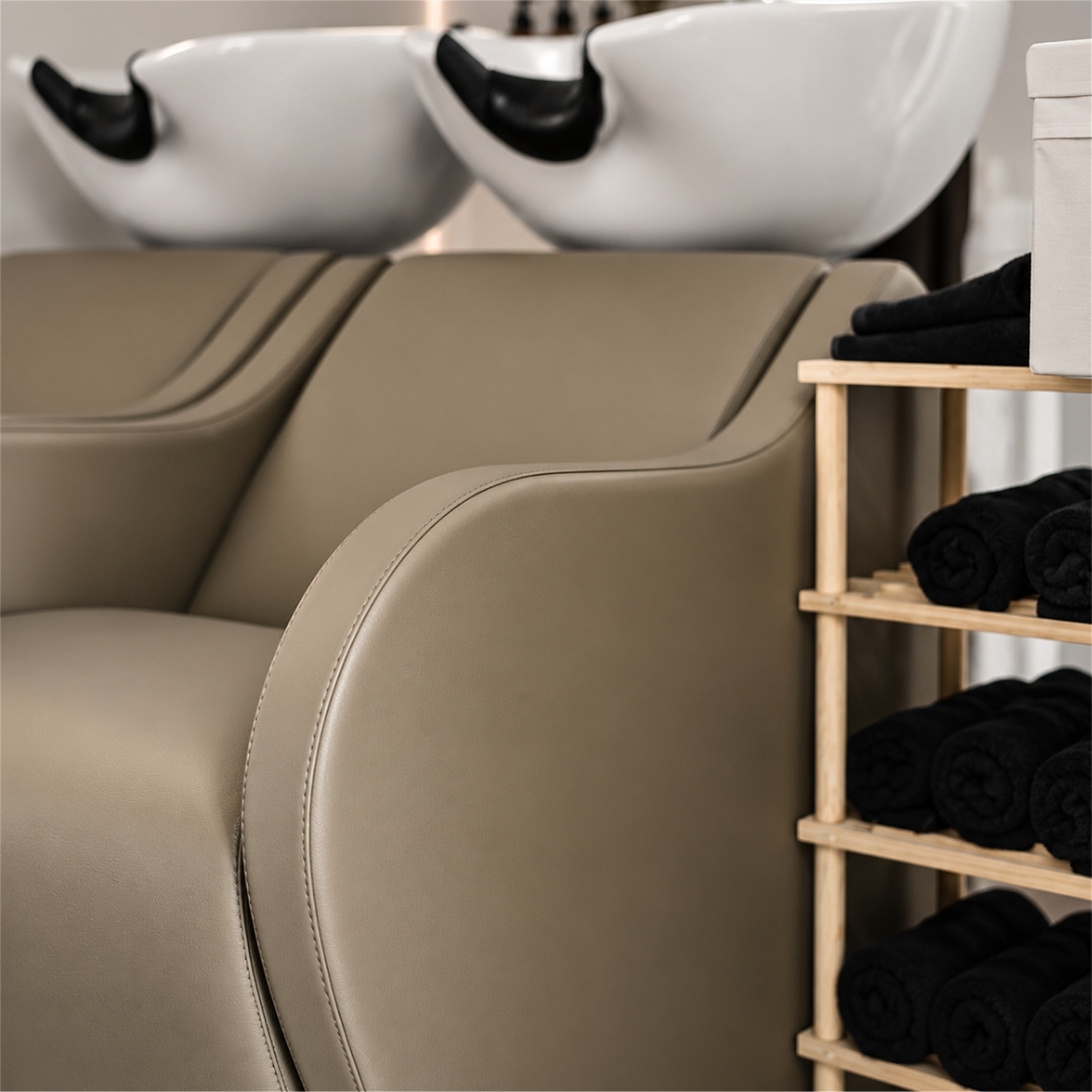 Lavacabezas con sillones reclinables taupe y una estantería con toallas negras enrolladas
